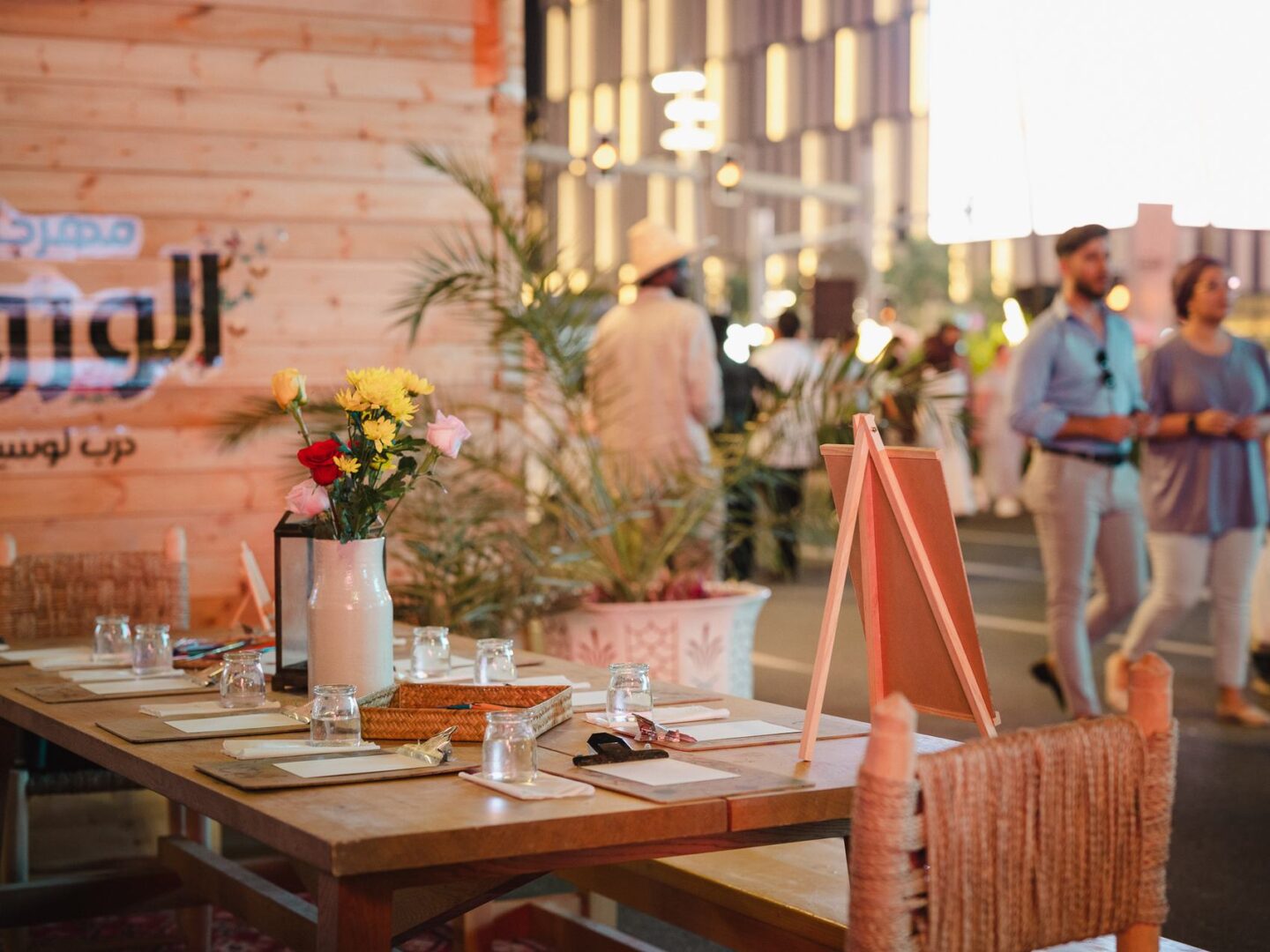 A long wooden table set with flowers and glassware beside a market stall