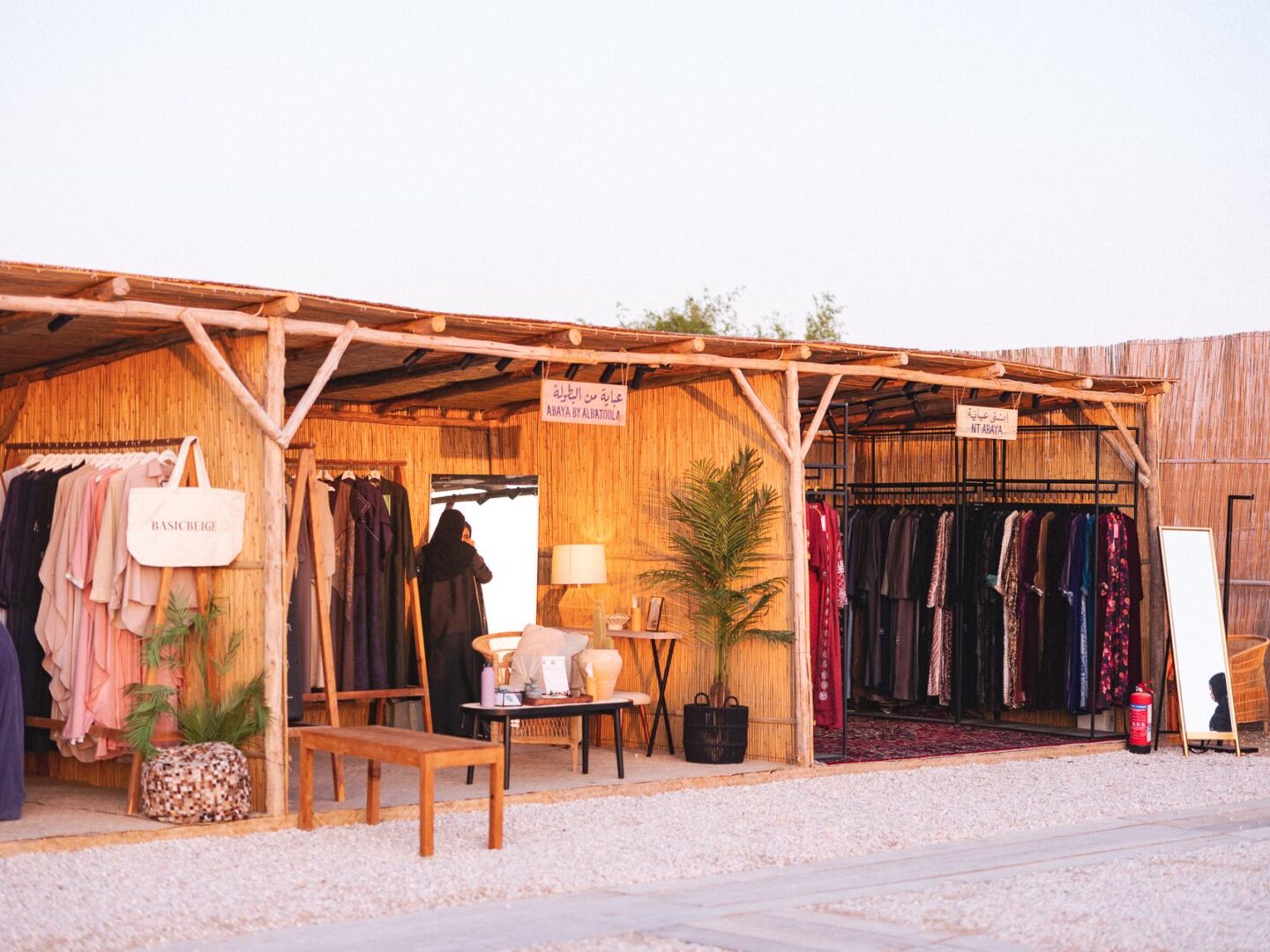 A market booth with a bamboo canopy, clothing rails, plants and a small wooden bench