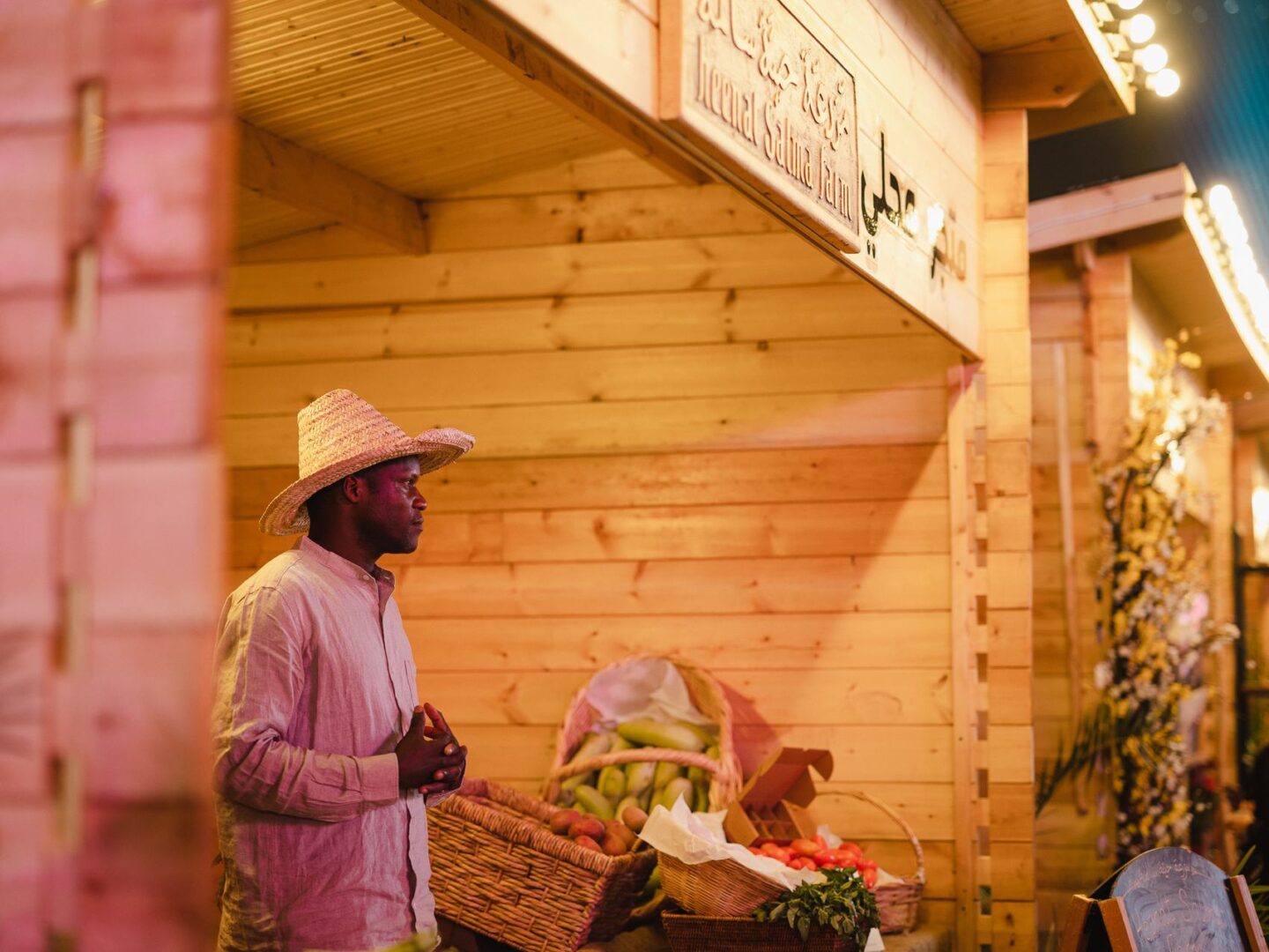 A vendor in a straw hat beside a basket of fresh fruit at a warmly lit wooden stall