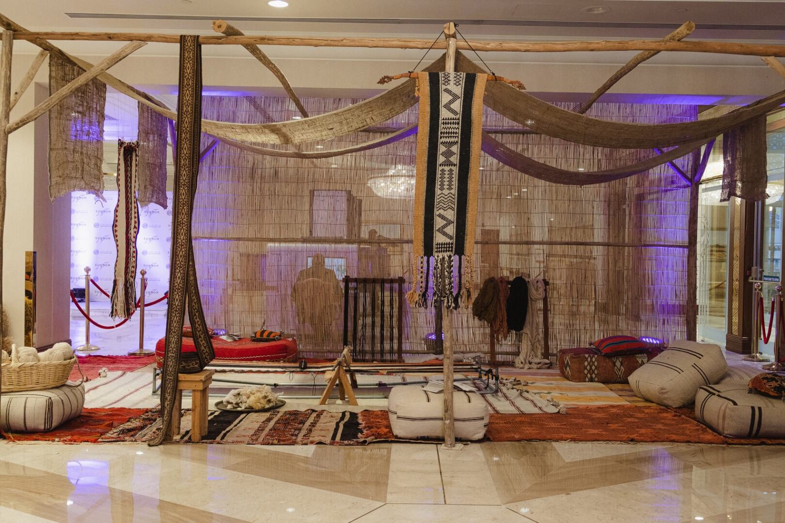 A weaving installation with a wooden loom, hanging textiles and floor cushions