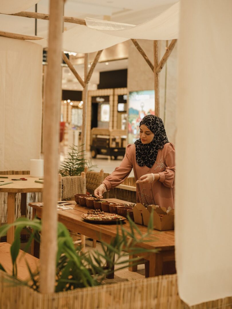 A woman arranging bowls of food at a bamboo market stall