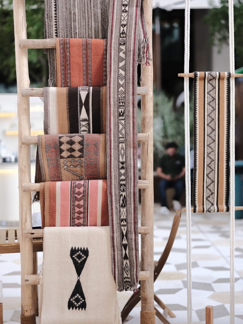 Handwoven textiles and rugs draped over a wooden ladder
