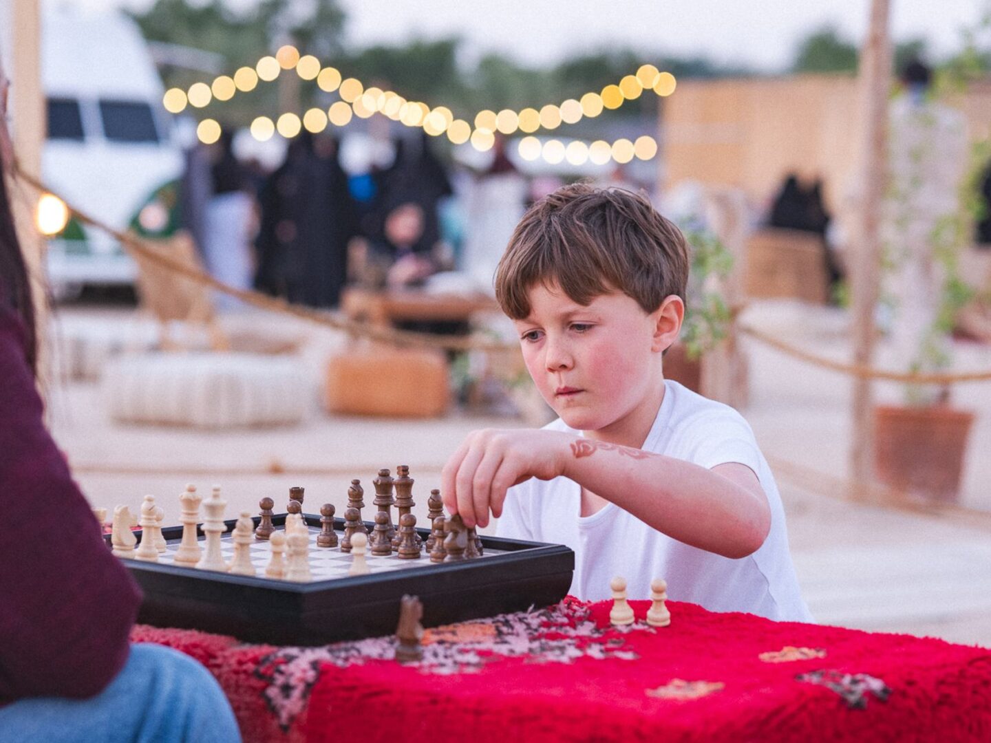 A boy playing chess on a red woven cloth at an outdoor market