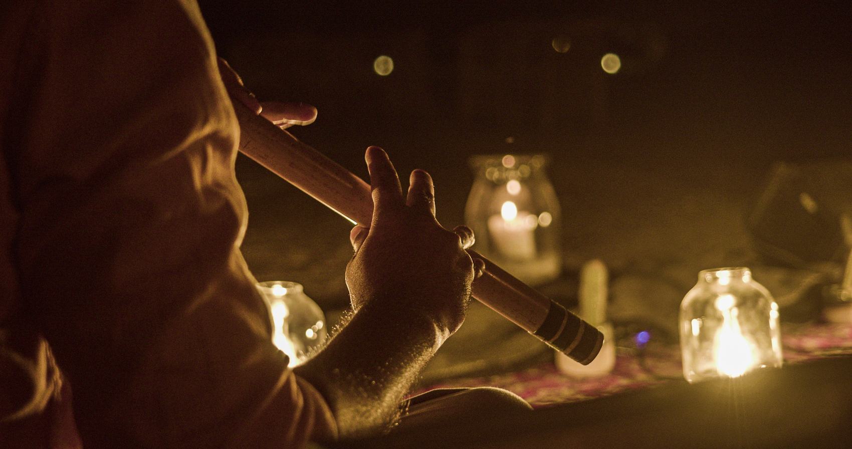 A musician playing a wooden flute beside glowing candle lanterns at night