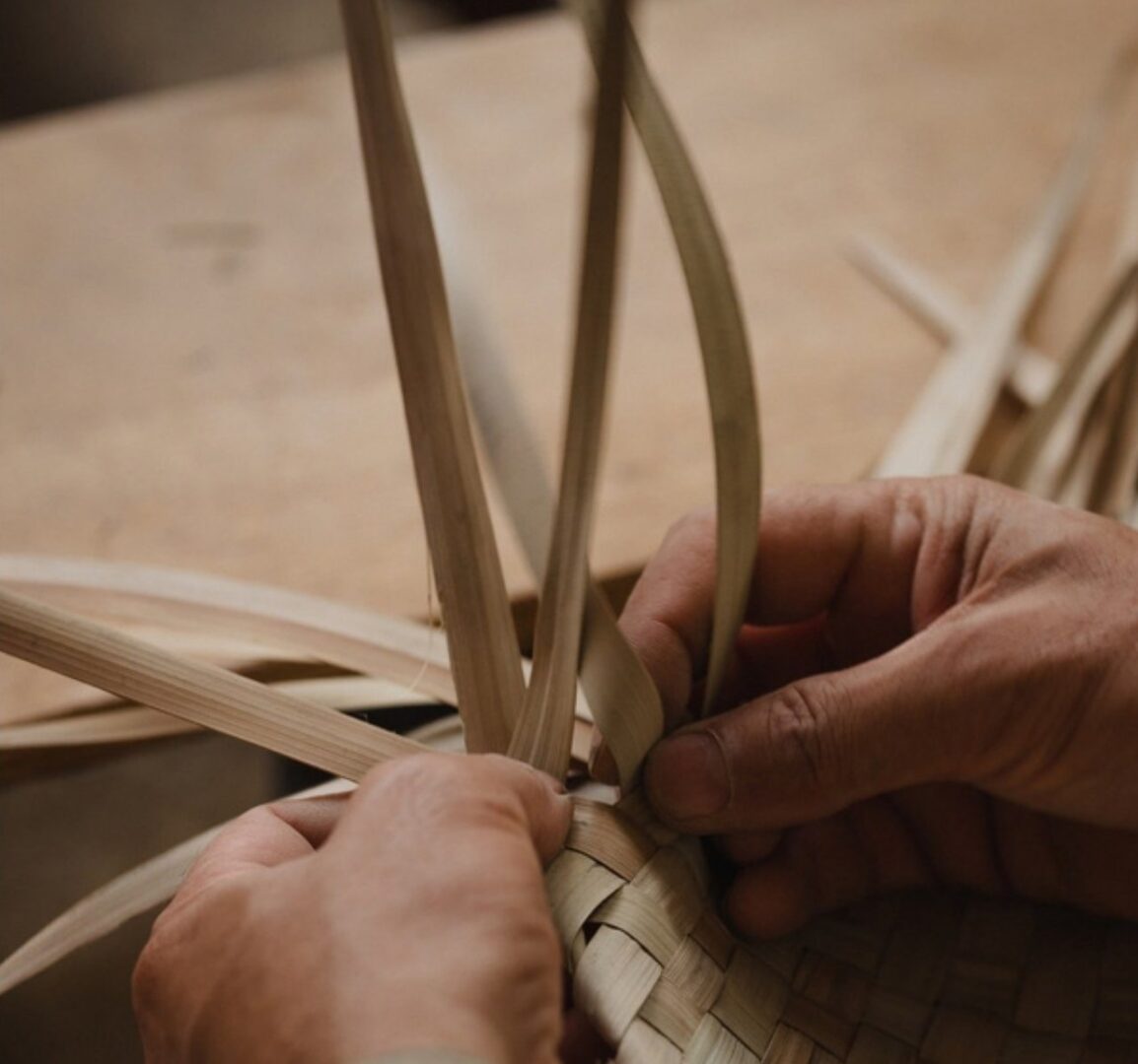 Hands weaving strips of dried palm leaf in an artisanal workshop