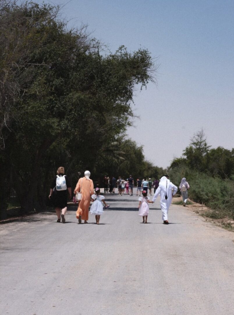 Families walking along a tree-lined road at Heenat Salma Farm