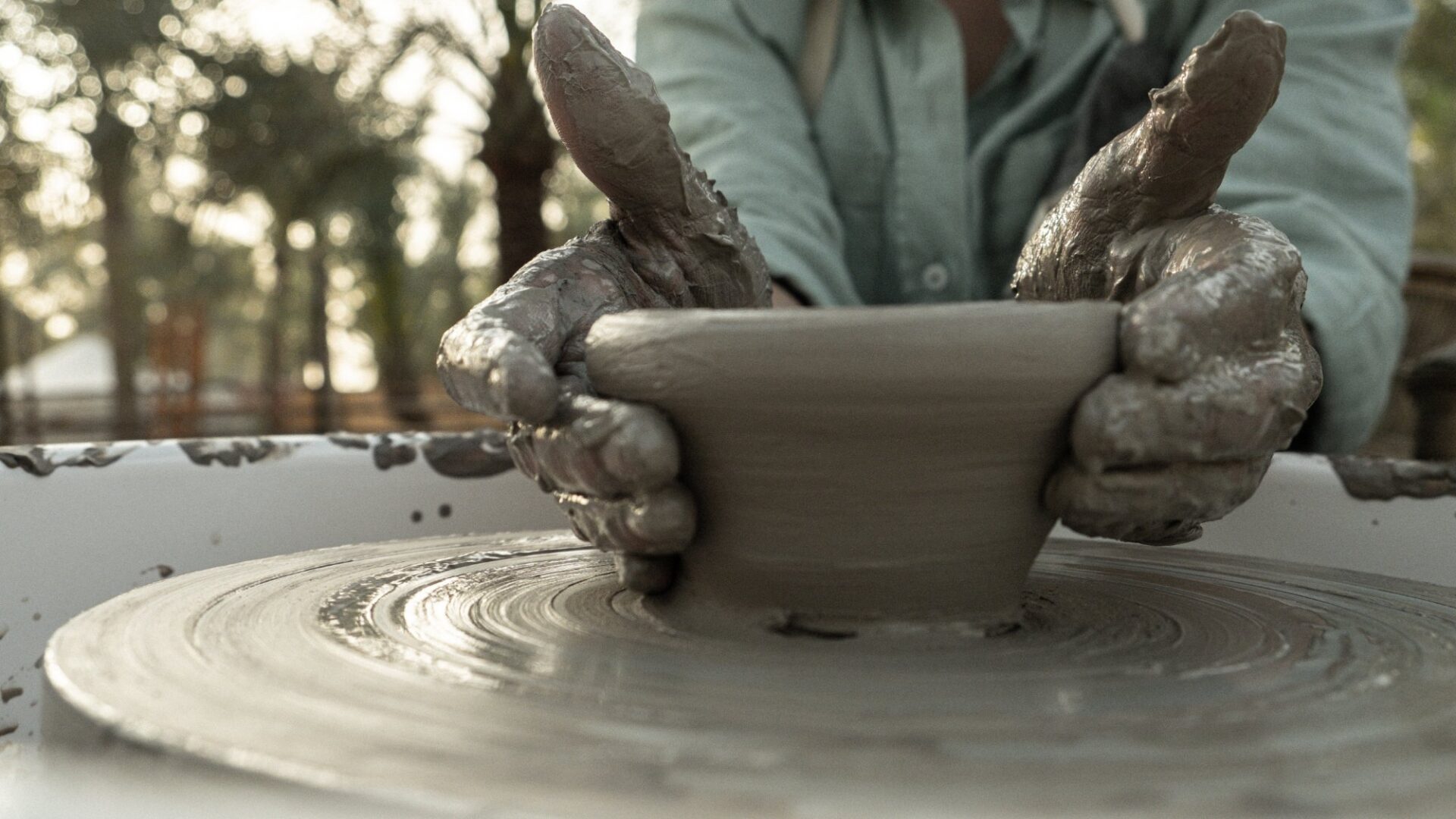 Clay-covered hands shaping a bowl on a pottery wheel