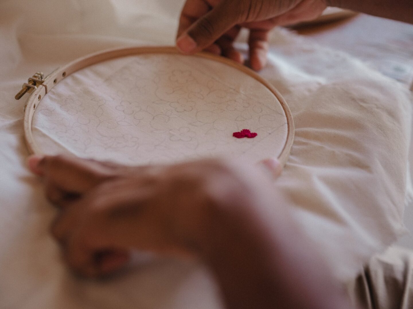 Hands stitching thread through fabric on an embroidery hoop