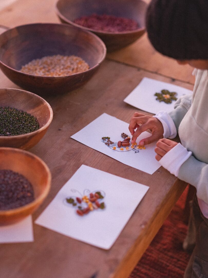 Hands arranging seeds and grains on cards beside clay bowls