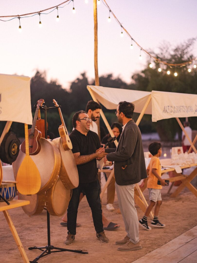 Musicians with an oud and drums under string lights at dusk