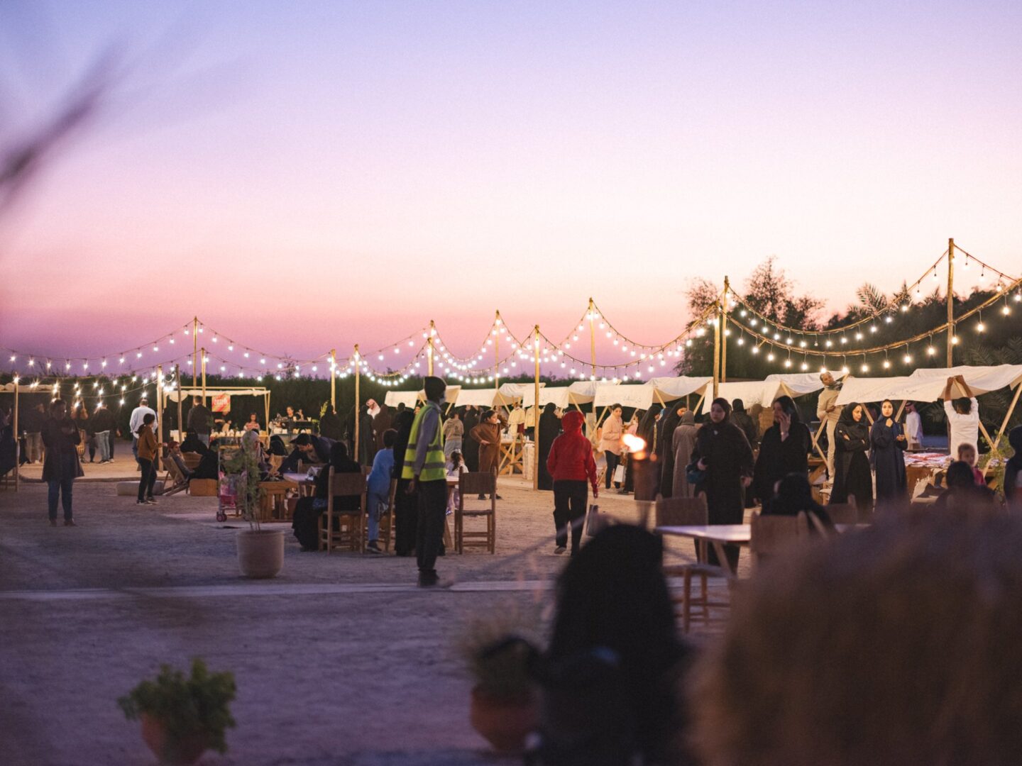 Visitors walking between the lit stalls of the Winter Bazaar at dusk